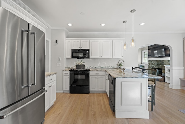 kitchen featuring a peninsula, a fireplace, a kitchen breakfast bar, white cabinets, and black appliances