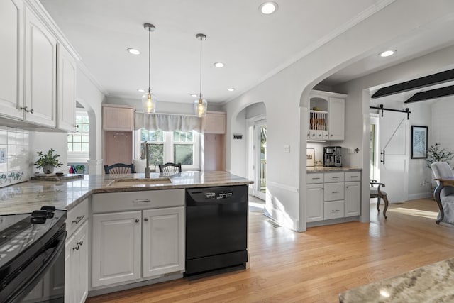 kitchen featuring black appliances, a sink, a barn door, a peninsula, and light wood finished floors