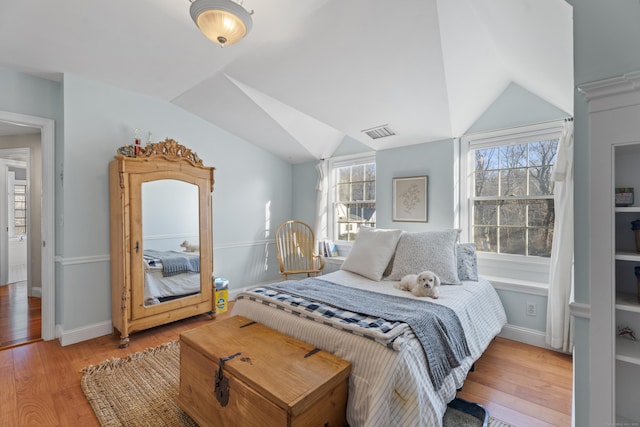 bedroom with light wood-type flooring, visible vents, baseboards, and vaulted ceiling