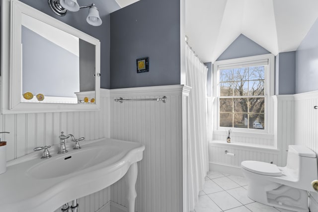 full bathroom with tile patterned floors, toilet, lofted ceiling, and wainscoting