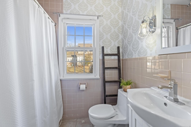 full bath featuring a wainscoted wall, wallpapered walls, tile patterned floors, toilet, and tile walls