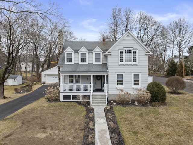 traditional-style house featuring a front lawn, a porch, a shingled roof, a garage, and a chimney