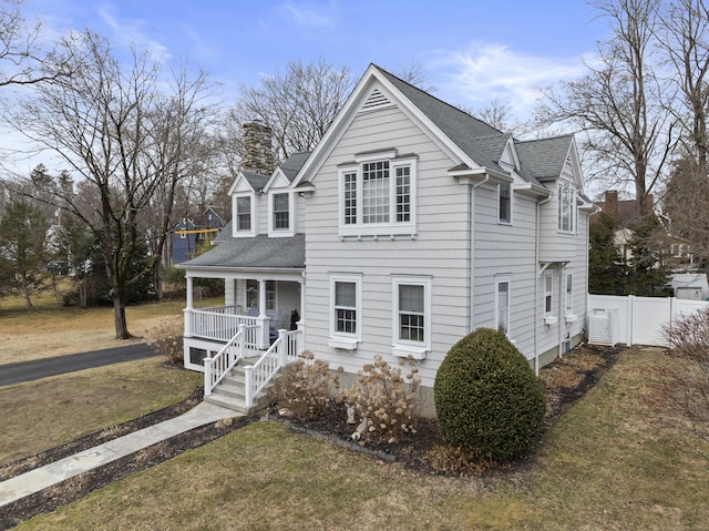 view of front of property featuring a porch, fence, roof with shingles, a front yard, and a chimney