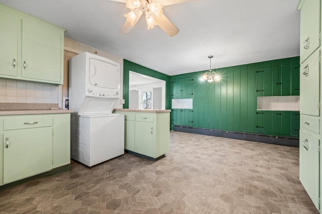 clothes washing area with a baseboard radiator, cabinet space, stacked washer and dryer, tile patterned floors, and ceiling fan with notable chandelier