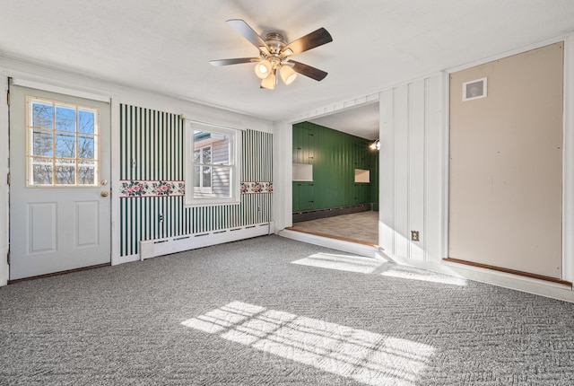 empty room with carpet, visible vents, a ceiling fan, a baseboard heating unit, and baseboard heating