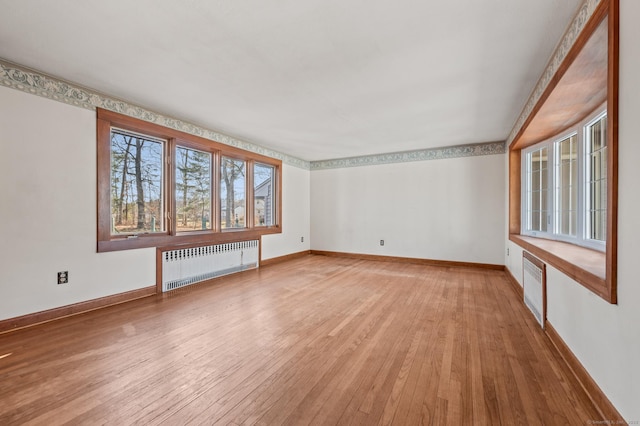 unfurnished room featuring radiator, baseboards, and light wood finished floors