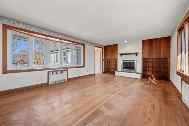 unfurnished living room with baseboards, a fireplace, radiator heating unit, and hardwood / wood-style flooring