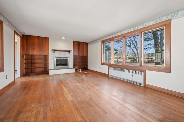 unfurnished living room featuring radiator, a fireplace, baseboards, and hardwood / wood-style floors