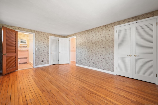 unfurnished bedroom with wallpapered walls, radiator heating unit, baseboards, and light wood-type flooring