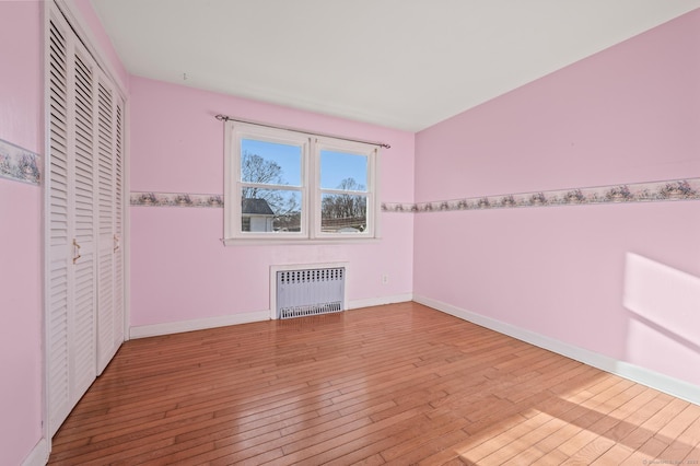 unfurnished bedroom featuring a closet, wood-type flooring, radiator, and baseboards