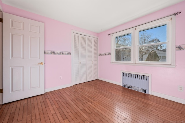 unfurnished bedroom featuring a closet, radiator, baseboards, and hardwood / wood-style flooring