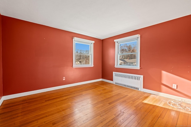 empty room featuring hardwood / wood-style flooring, radiator, and baseboards