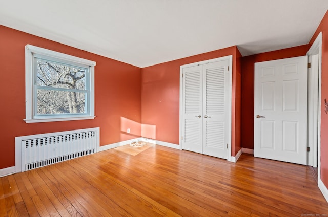 unfurnished bedroom featuring radiator, baseboards, a closet, and wood-type flooring