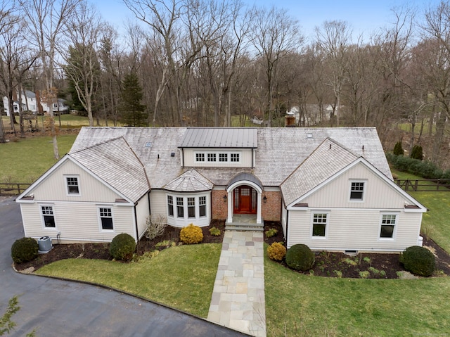 view of front of home with a standing seam roof, a front yard, and cooling unit