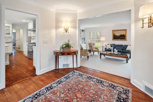 hallway with baseboards, visible vents, wood finished floors, and ornamental molding