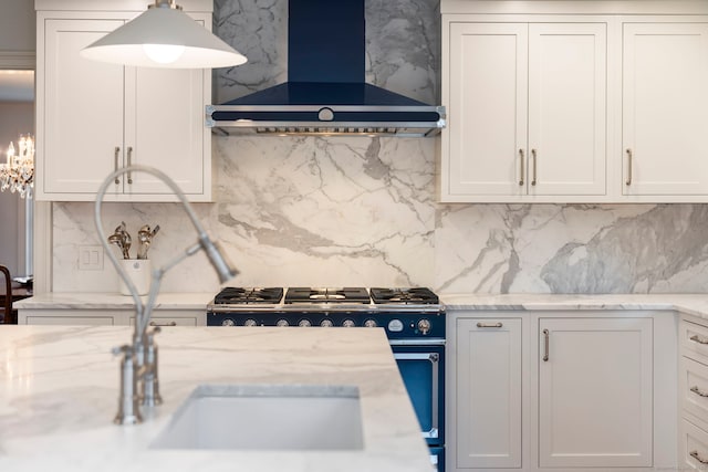 kitchen with white cabinets, wall chimney range hood, tasteful backsplash, and range with gas stovetop