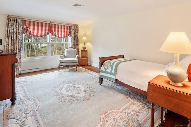 bedroom with a baseboard heating unit, baseboards, visible vents, and wood finished floors