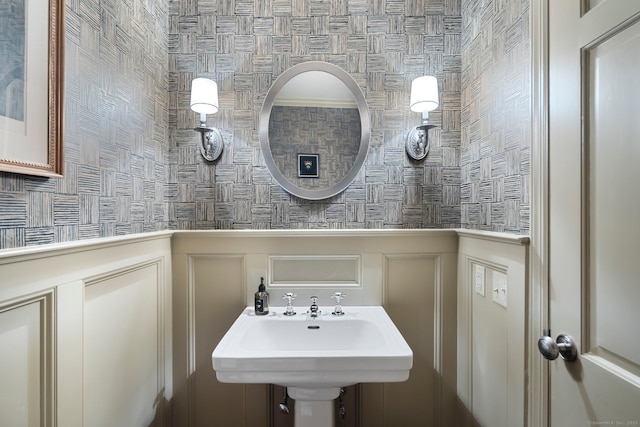 bathroom featuring a decorative wall, a sink, and wainscoting