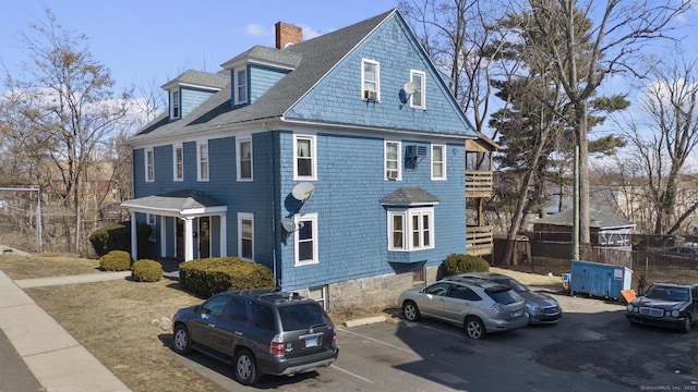 view of property exterior with a shingled roof, uncovered parking, and a chimney