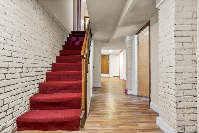 stairs with a baseboard radiator, brick wall, baseboards, and wood finished floors