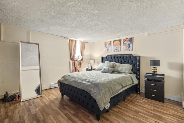 bedroom featuring a textured ceiling, a baseboard heating unit, and wood finished floors