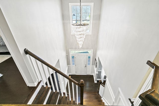 staircase with a chandelier, wood finished floors, a towering ceiling, and baseboards