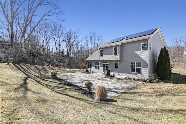 back of house with roof mounted solar panels, a patio area, and a lawn