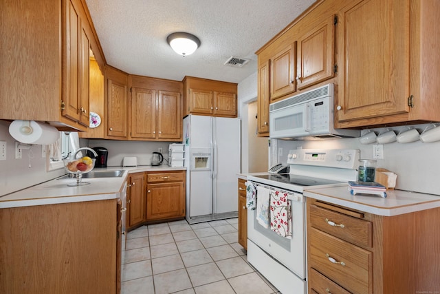 kitchen featuring white appliances, light tile patterned floors, visible vents, brown cabinetry, and light countertops