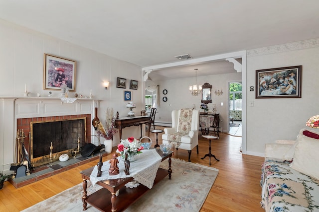 living area featuring light wood finished floors, visible vents, baseboard heating, a brick fireplace, and a notable chandelier