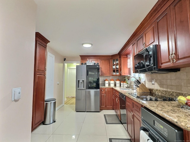 kitchen with light tile patterned floors, decorative backsplash, a sink, light stone countertops, and black appliances