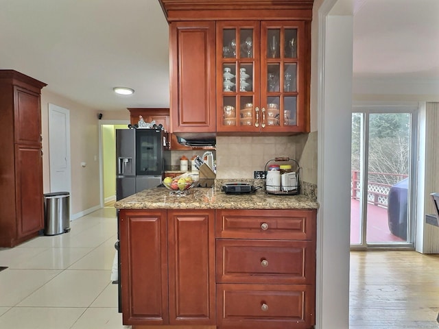 kitchen with light stone countertops, backsplash, glass insert cabinets, and stainless steel fridge with ice dispenser