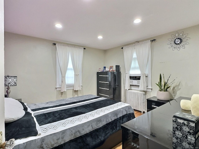 bedroom with multiple windows, radiator heating unit, wood finished floors, and recessed lighting