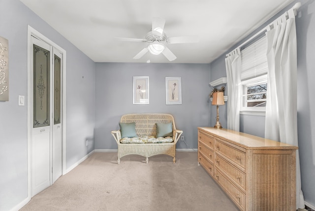 living area with baseboards, a ceiling fan, and light colored carpet