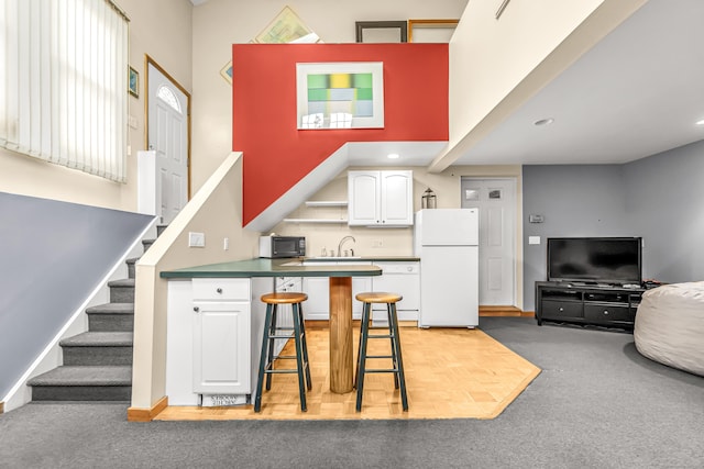 kitchen featuring a breakfast bar area, white cabinetry, white appliances, a peninsula, and baseboards