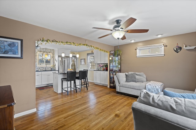 living area featuring baseboards, ceiling fan, and light wood-style floors