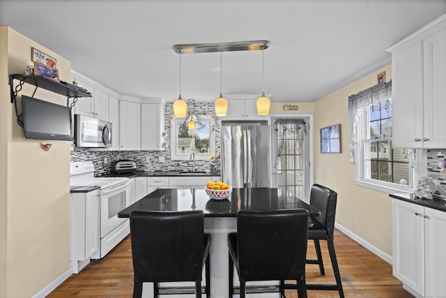 kitchen featuring dark wood finished floors, dark countertops, appliances with stainless steel finishes, a sink, and backsplash