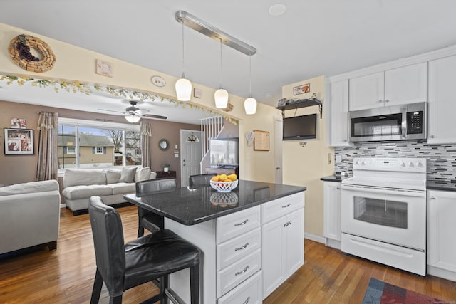 kitchen with white range with electric stovetop, decorative backsplash, dark wood-style floors, stainless steel microwave, and a breakfast bar area