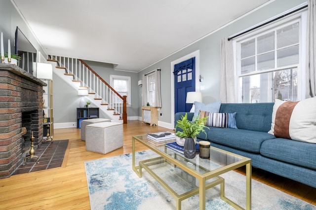 living area with wood finished floors, baseboards, a fireplace, ornamental molding, and stairs