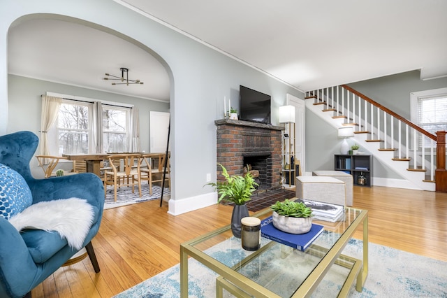 living room with wood finished floors, baseboards, arched walkways, stairs, and crown molding