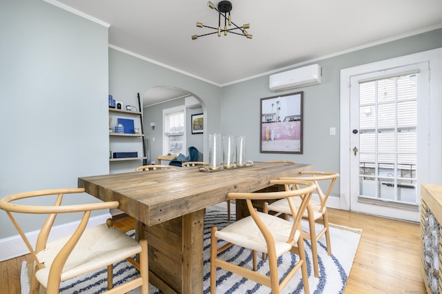 dining area with an AC wall unit, arched walkways, an inviting chandelier, crown molding, and light wood finished floors