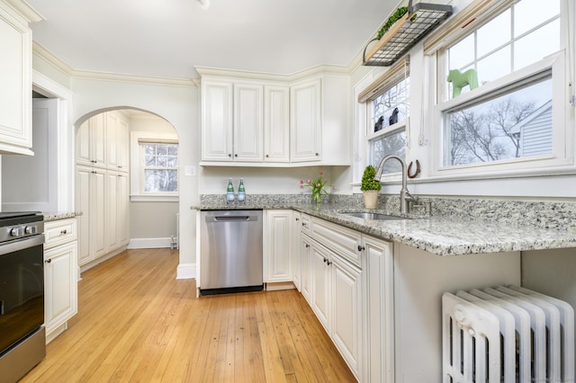 kitchen with a sink, radiator heating unit, stainless steel appliances, arched walkways, and light wood-style floors