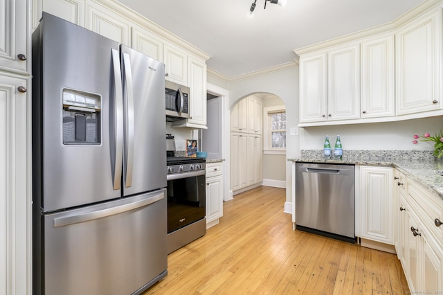 kitchen with ornamental molding, light stone counters, light wood-style flooring, appliances with stainless steel finishes, and arched walkways