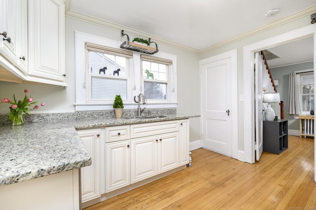 kitchen featuring a sink, light wood-style flooring, white cabinets, and crown molding