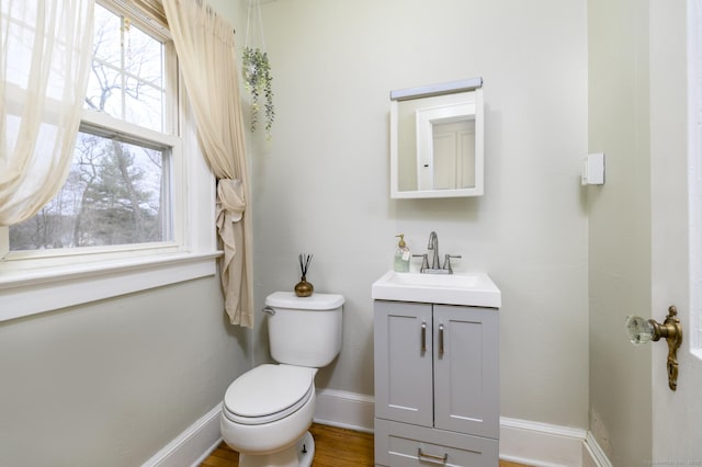 half bathroom with baseboards, toilet, wood finished floors, and vanity