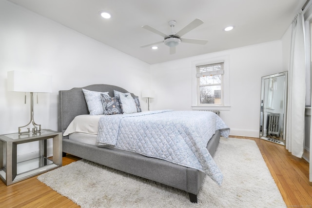 bedroom featuring radiator, wood finished floors, recessed lighting, and baseboards