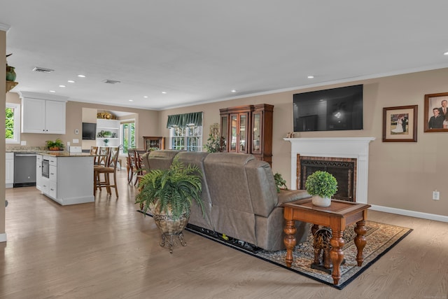 living area featuring plenty of natural light, crown molding, light wood-type flooring, and a brick fireplace