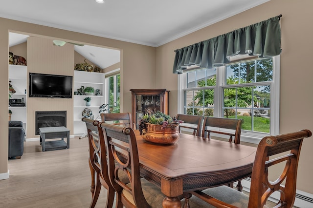 dining space featuring light wood finished floors, a glass covered fireplace, lofted ceiling, a baseboard radiator, and crown molding