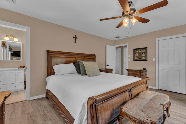 bedroom featuring light wood finished floors, visible vents, ensuite bathroom, a sink, and baseboards