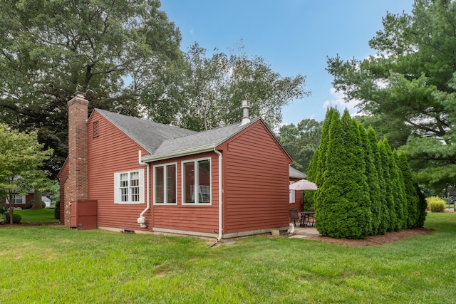 view of side of home with a yard, a shingled roof, a chimney, and a patio