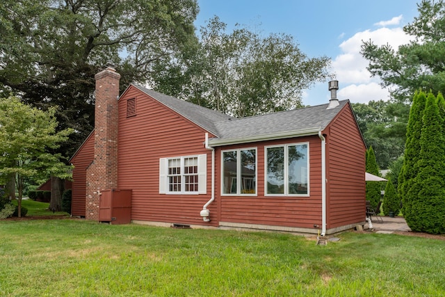 back of property with a shingled roof, a chimney, and a yard